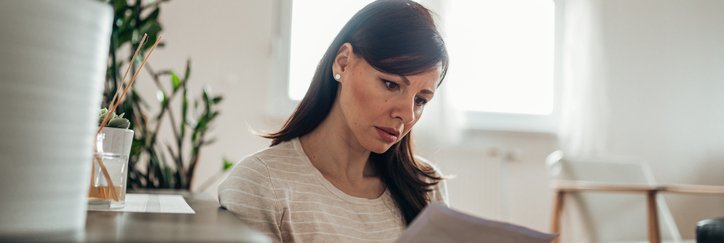 A worried-looking woman reading a letter in her home.