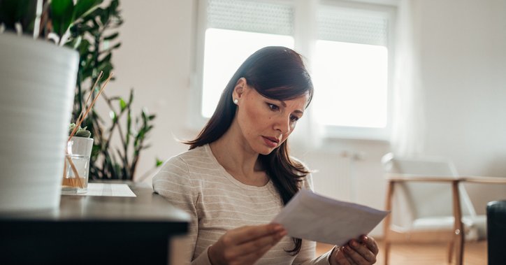 A worried-looking woman reading a letter in her home.