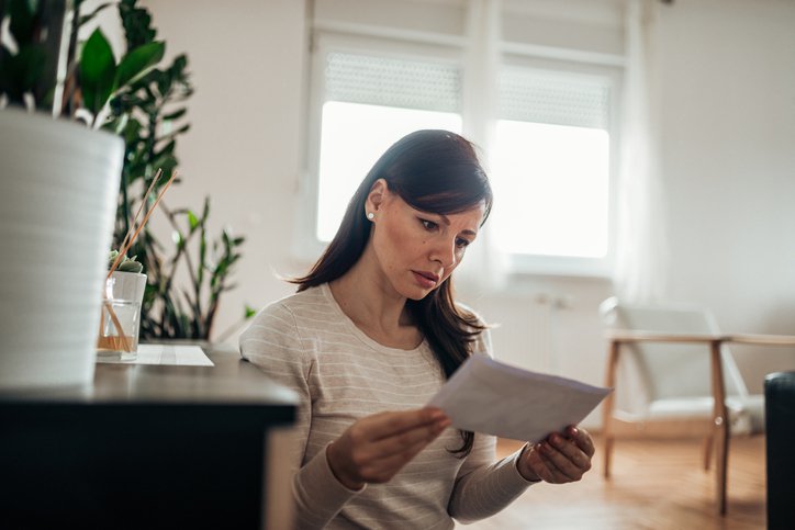 A worried-looking woman reading a letter in her home.