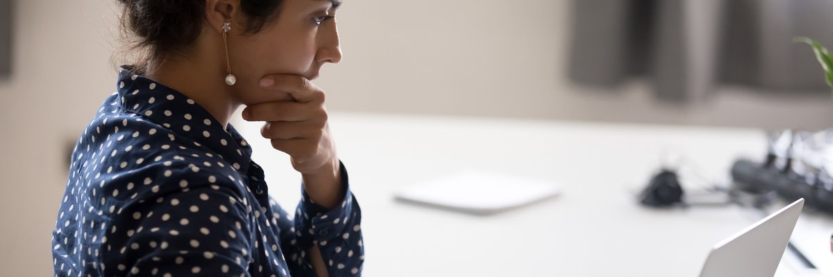 A worried woman with her hand on her chin sitting at a desk with papers and her laptop.