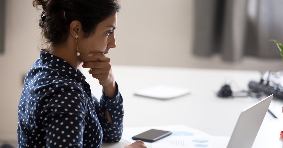 A worried woman with her hand on her chin sitting at a desk with papers and her laptop.
