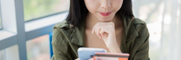 young woman holding credit card and smartphone and thinking with chin on fist