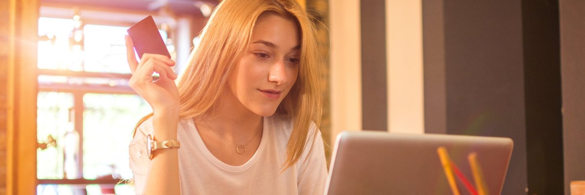 Young adult woman at laptop holding credit card.