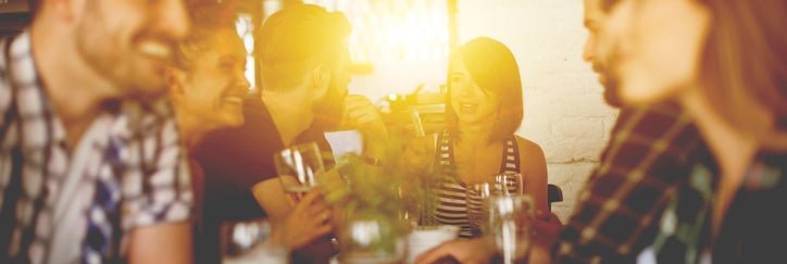 A group of young adults sitting at a table in a sunny bar enjoying beers and chatting.
