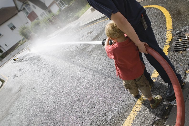 A young boy and a fireman practicing how to use a fire hose.