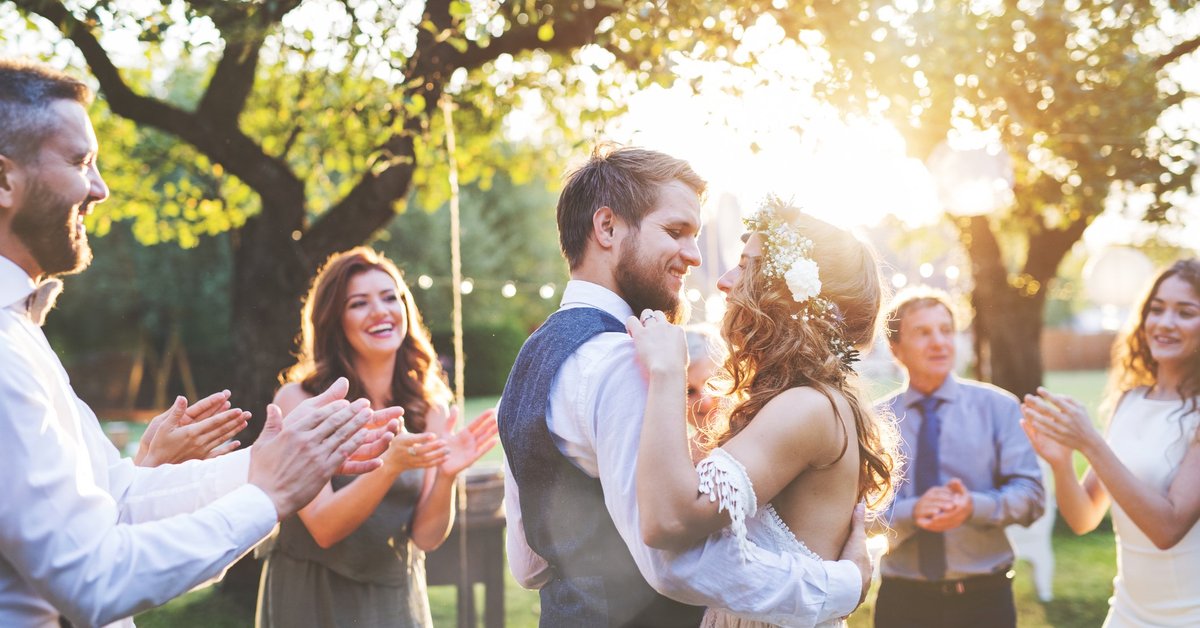 young bride and groom hugging in a backyard surrounded by friends