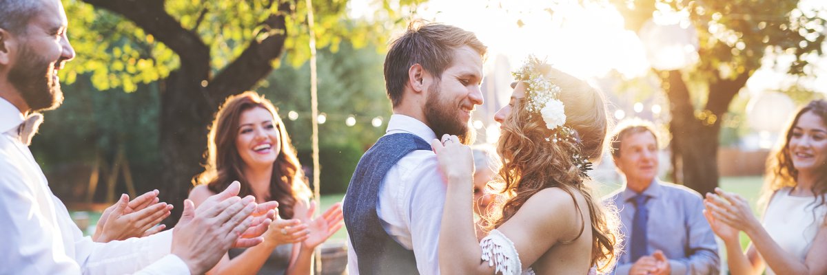 young bride and groom hugging in a backyard surrounded by friends