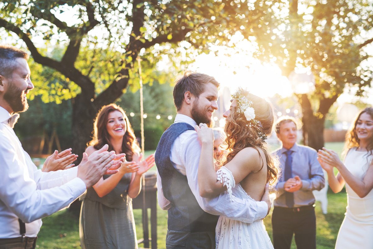 young bride and groom hugging in a backyard surrounded by friends