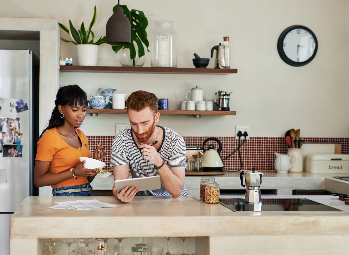A young couple standing in their kitchen and looking things up on a tablet.