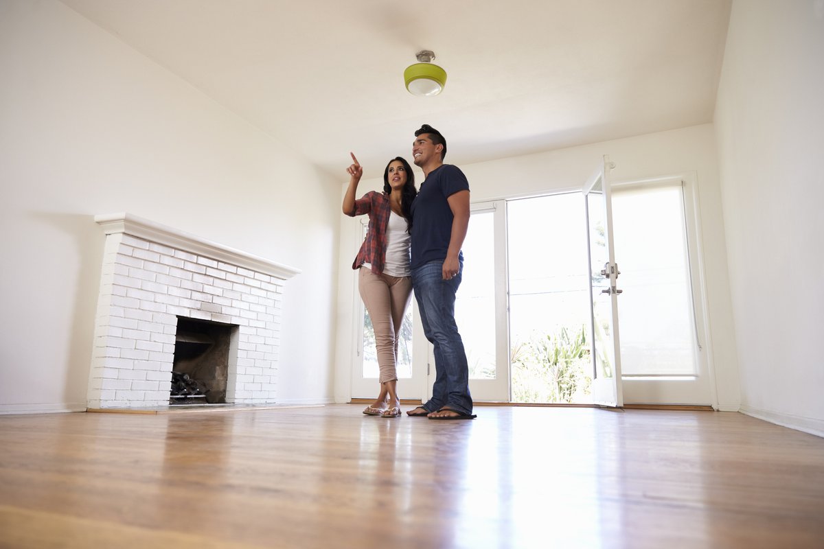 A young couple walking through an empty living room on a house tour.