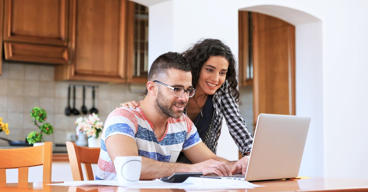 A young couple looking up information on a laptop while sitting in their kitchen.