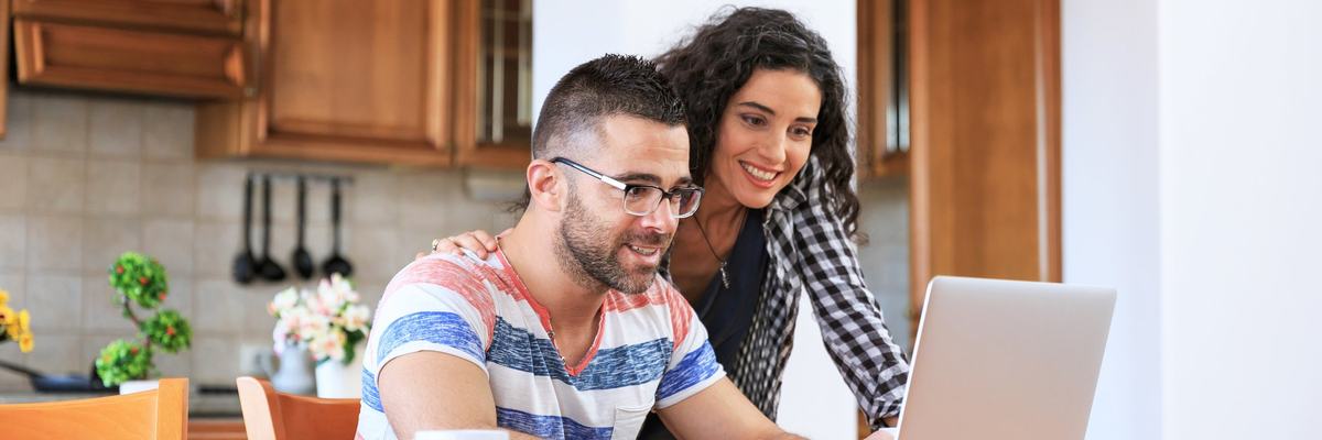A young couple looking up information on a laptop while sitting in their kitchen.