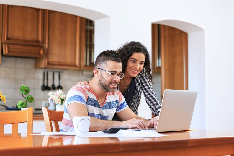 A young couple looking up information on a laptop while sitting in their kitchen.