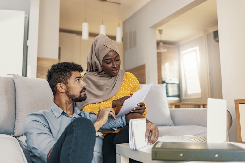A stressed young couple looking over their bills while sitting in their large living room.