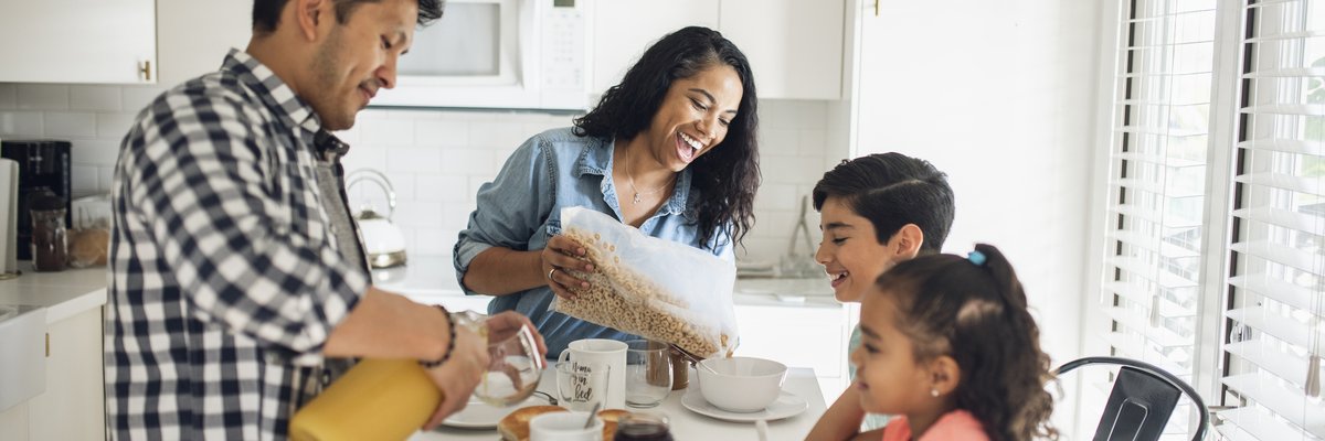 Two parents making breakfast for their young kids sitting in the kitchen.