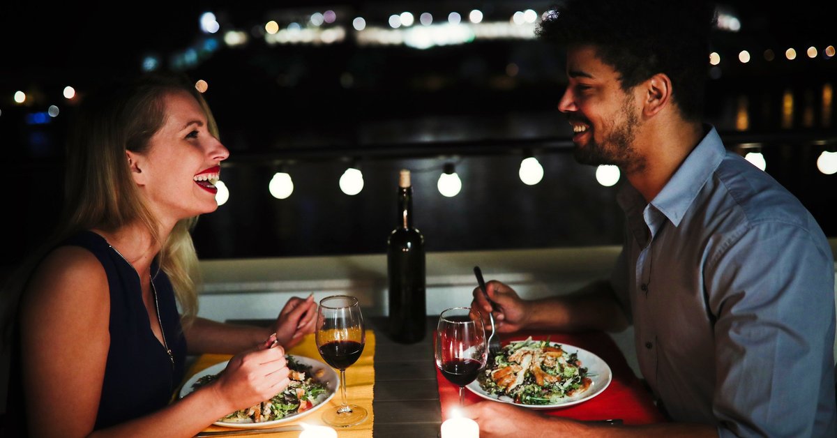 Young man and woman sitting at table eating dinner and laughing.