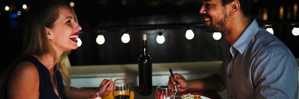 Young man and woman sitting at table eating dinner and laughing.