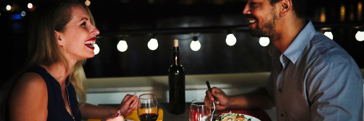 Young man and woman sitting at table eating dinner and laughing.