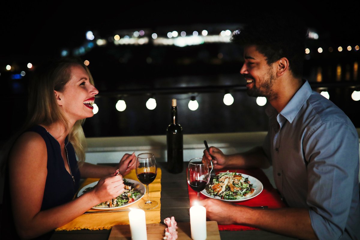 Young man and woman sitting at table eating dinner and laughing.