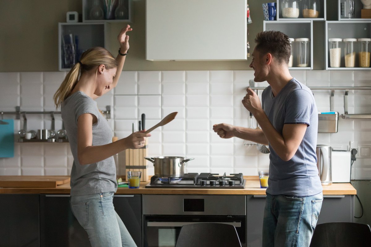 young man and woman smiling and dancing in kitchen -- couple celebrating happy