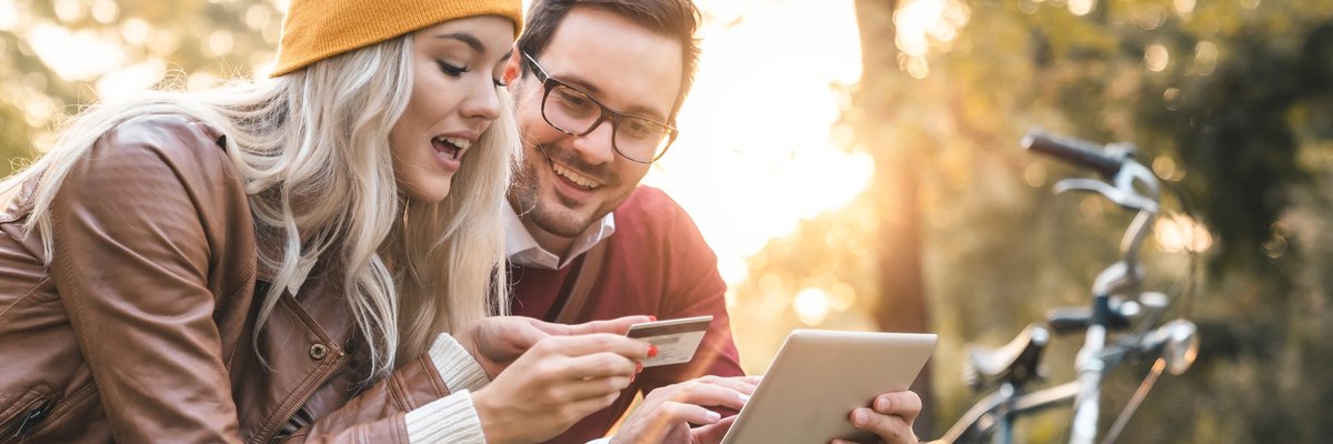 young man and woman with shopping bags looking at a credit card and a tablet.