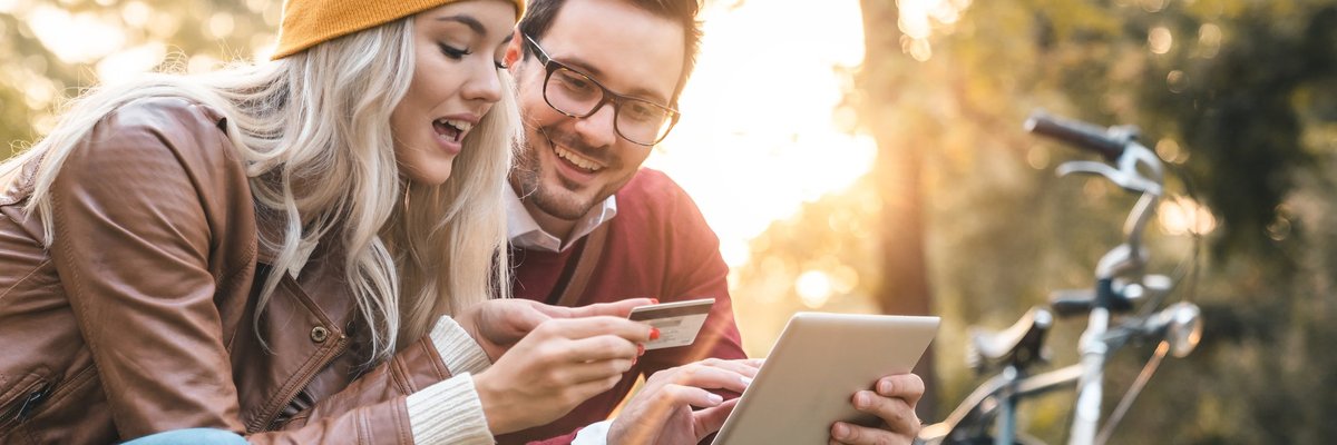young man and woman with shopping bags looking at a credit card and a tablet.
