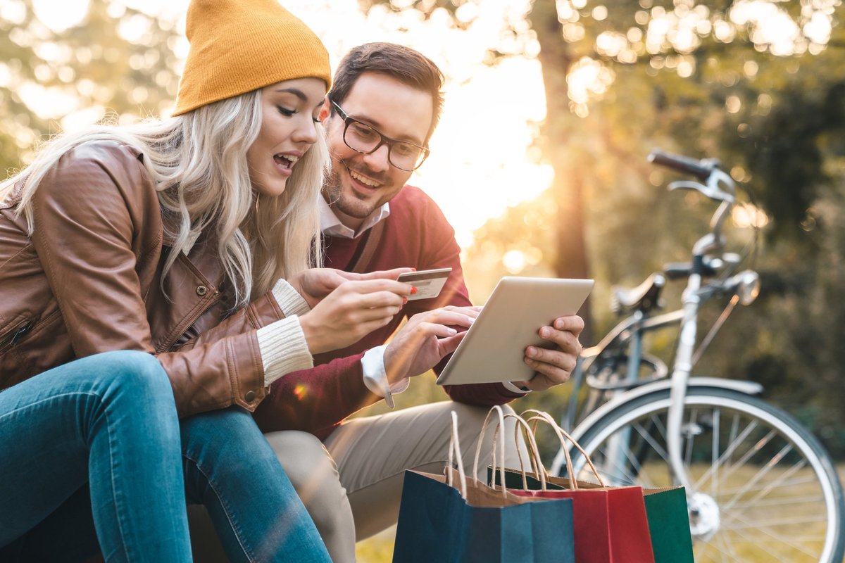 young man and woman with shopping bags looking at a credit card and a tablet.