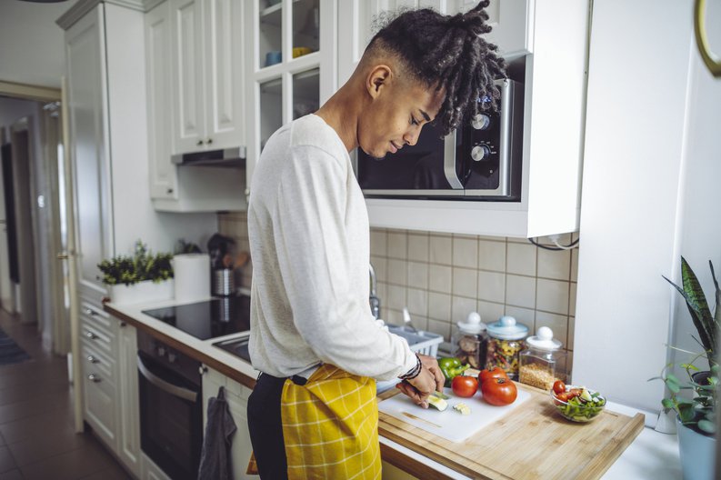 A young man chopping vegetables in his kitchen.