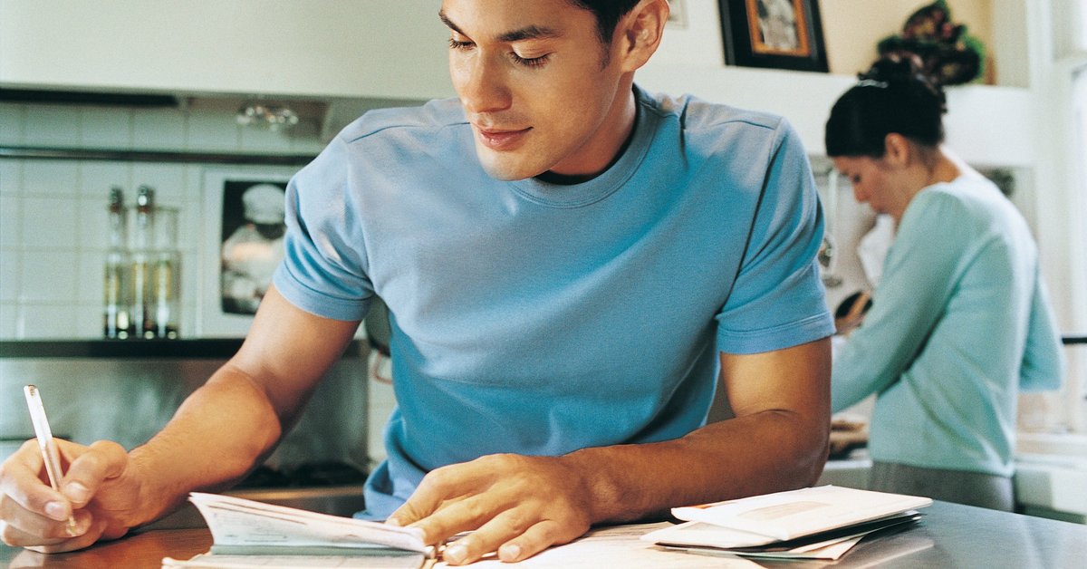 young man sitting at kitchen table writing a check
