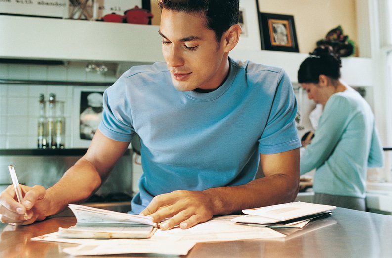 young man sitting at kitchen table writing a check.