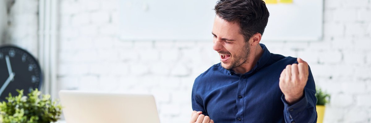 young man sitting in front of laptop and pumping his fist -- happy celebrating success