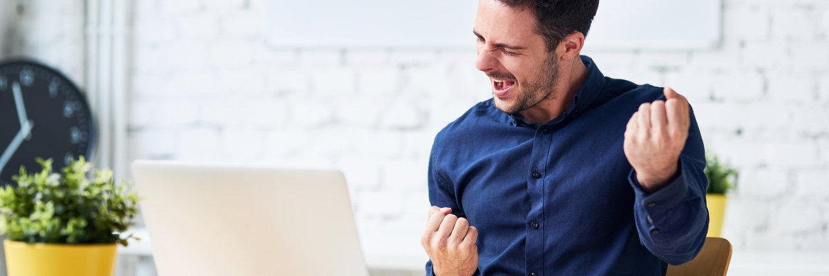 young man sitting in front of laptop and pumping his fist -- happy celebrating success