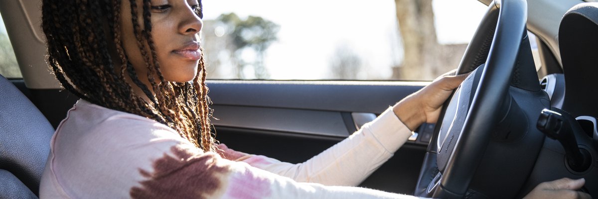 A young adult turning the key in the ignition of a car.