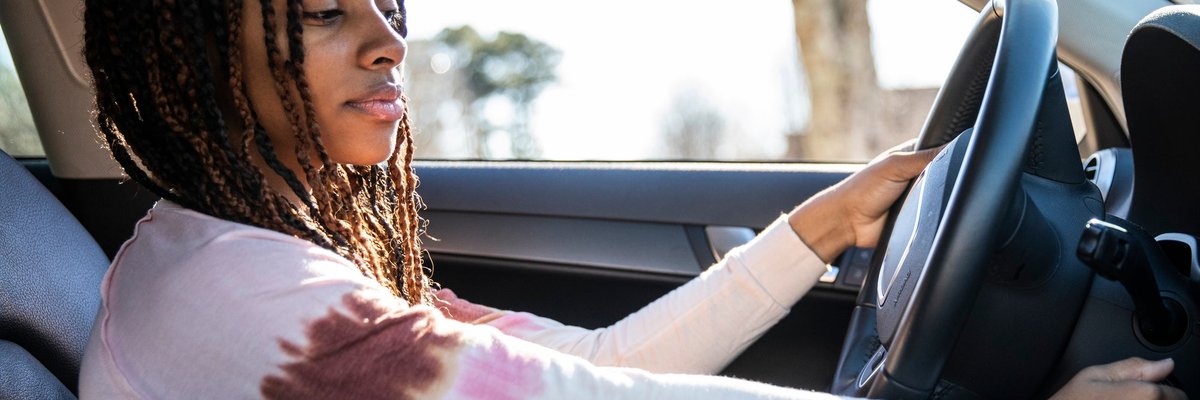A young adult turning the key in the ignition of a car.