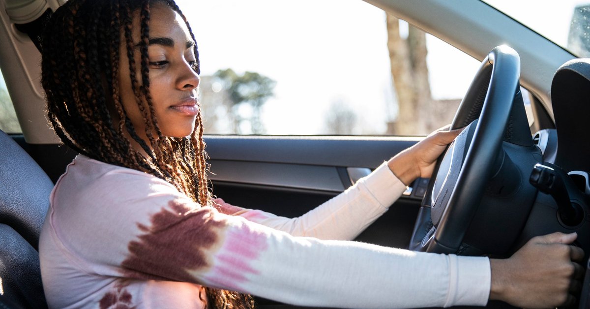 A young adult turning the key in the ignition of a car.