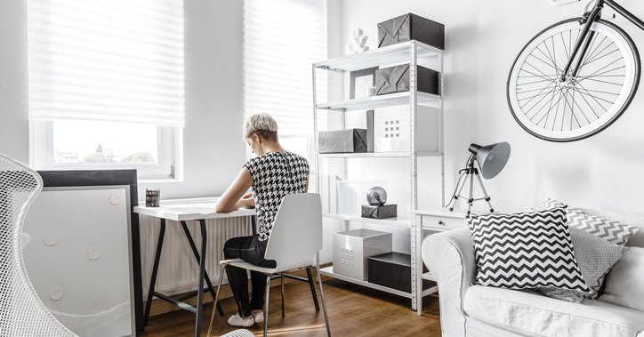 A young woman working at a small desk in the living room of her apartment.