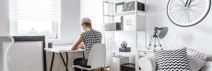 A young woman working at a small desk in the living room of her apartment.
