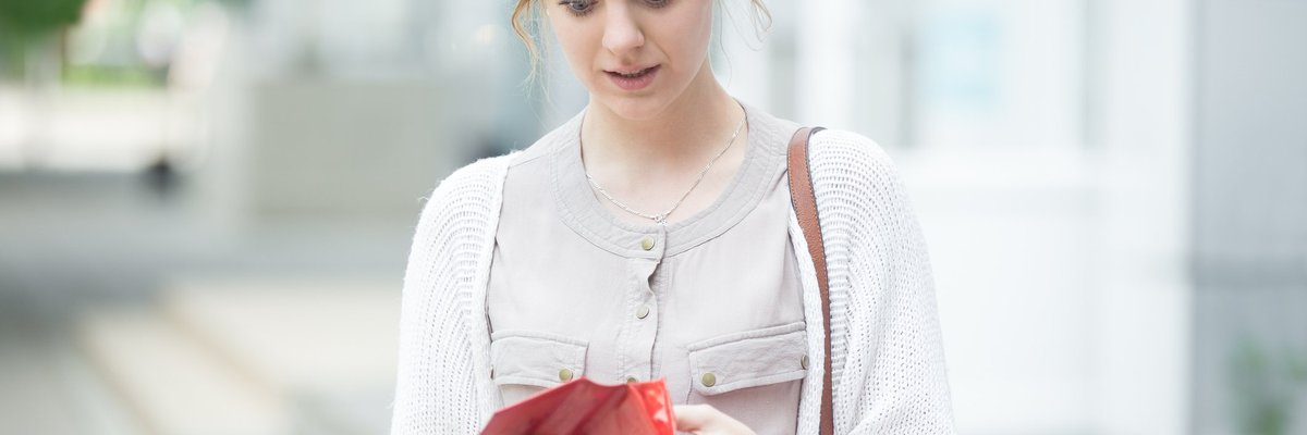 Young woman carrying shopping bags and looking into wallet with concern.
