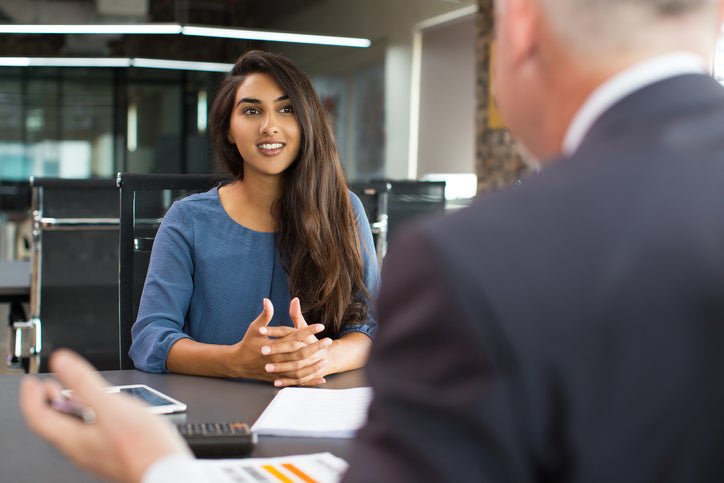 A young woman sitting across the table from a man in an office for a job interview.