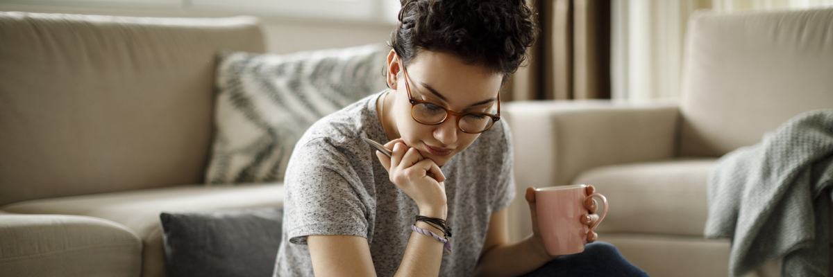 A young woman sitting on the floor of her living room with her laptop and bills around her.