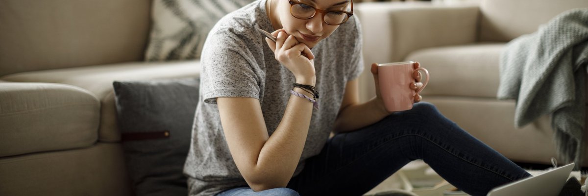 A young woman sitting on the floor of her living room with her laptop and bills around her.
