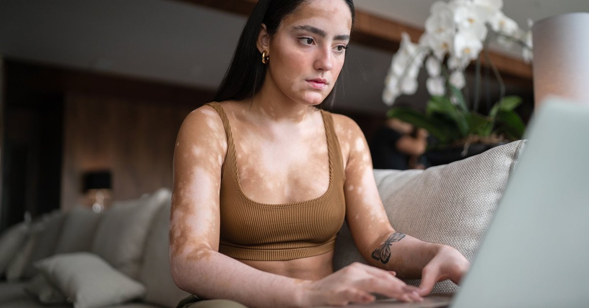 A young woman sits on her couch, reading the days news on her computer.