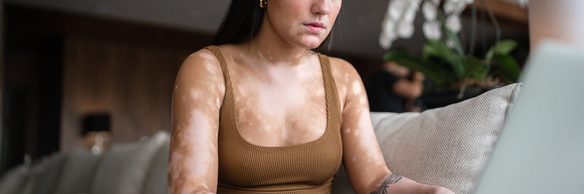 A young woman sits on her couch, reading the days news on her computer.