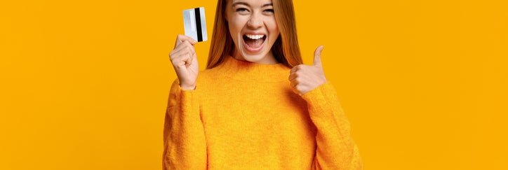 A young woman gives the thumbs-up sign while holding a credit card.
