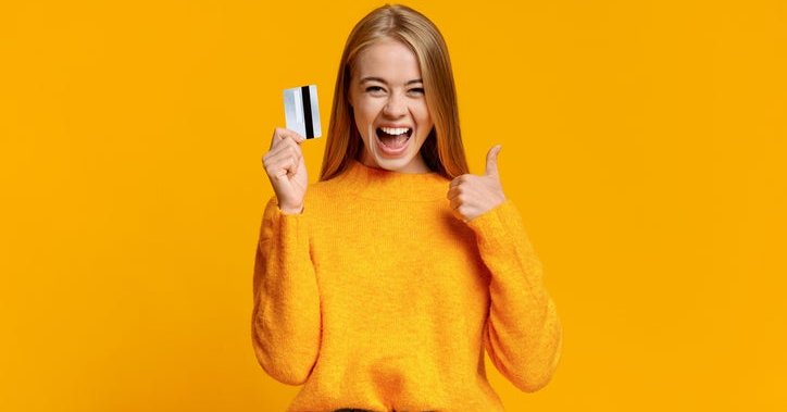 A young woman gives the thumbs-up sign while holding a credit card.