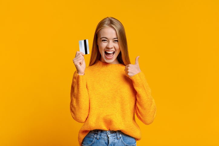 A young woman gives the thumbs-up sign while holding a credit card.