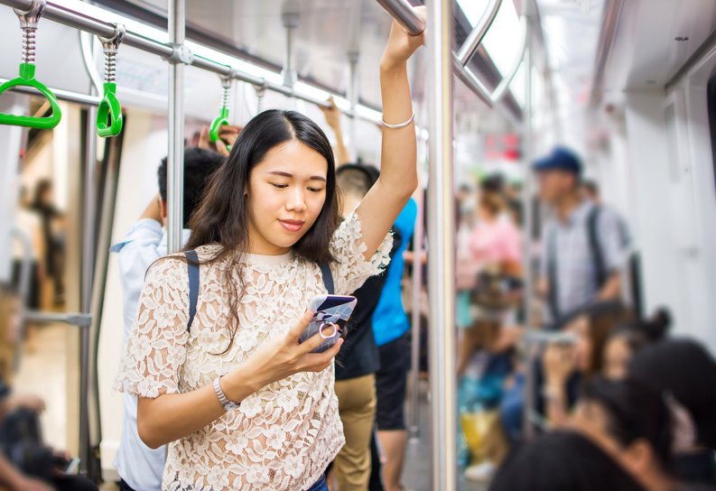 A young woman looking at her cell phone while riding public transportation.