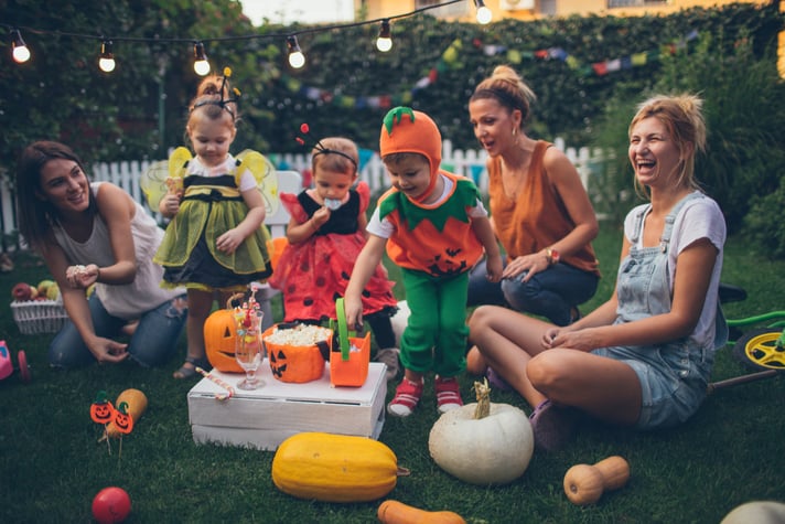 Adult women in Halloween costumes hold a gathering of children outdoors.