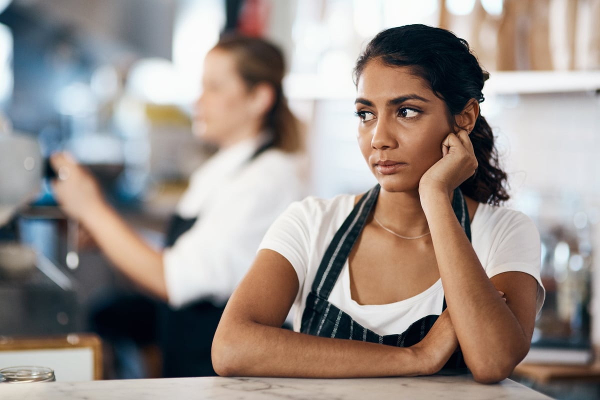 A barista stands behind the counter, looking unhappy.