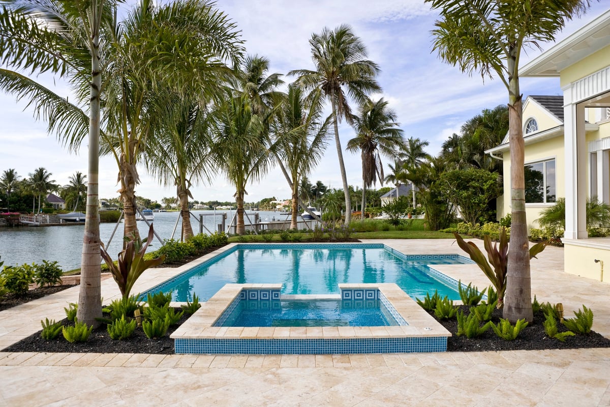 A backyard pool surrounded by palm trees in front of a winding lagoon.